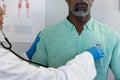 Biracial female doctor using stethoscope and examinating african american male patient