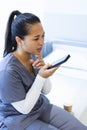 Biracial female doctor wearing scrubs talking on smartphon on bed in hospital