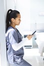 Biracial female doctor wearing scrubs using smartphon in hospital