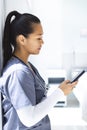 Biracial female doctor wearing scrubs using smartphon in hospital