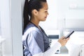 Biracial female doctor wearing scrubs using smartphon in hospital