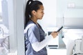 Biracial female doctor wearing scrubs using smartphon in hospital