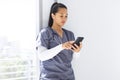 Biracial female doctor wearing scrubs using smartphon in hospital