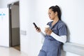 Biracial female doctor wearing scrubs using smartphone, holding takeaway coffee, copy space