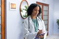 Biracial female doctor wearing stethoscope holding clipboard and taking notes at doctor's office Royalty Free Stock Photo