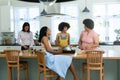 Biracial female friends talking and cooking food at kitchen island while enjoying weekend at home Royalty Free Stock Photo