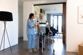 Biracial female physiotherapist assisting caucasian senior man in walking with walker at home Royalty Free Stock Photo