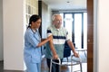 Biracial female physiotherapist assisting happy caucasian senior man in walking with walker at home Royalty Free Stock Photo
