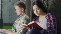 Biracial girl eagerly reading thrilling book without noticing guys loving looks