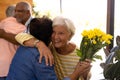 Biracial happy senior guests with bouquet embracing friends at entrance in nursing home Royalty Free Stock Photo