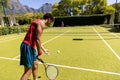Biracial man with racket bouncing ball to serve to player on sunny outdoor tennis court, copy space Royalty Free Stock Photo