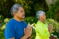 Biracial senior couple with eyes closed meditating in prayer positing while standing in yard Royalty Free Stock Photo