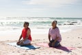 Biracial senior couple meditating while kneeling on yoga mats at beach against sky during sunny day