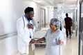 Biracial senior female patient with drip shaking hand of happy diverse male doctor in corridor