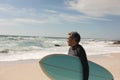 Biracial senior man carrying surfboard looking at sea against sky from beach on sunny day