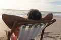 Biracial senior man relaxing with hands behind head sitting on folding chair at beach during sunset Royalty Free Stock Photo