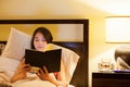 Biracial teen girl reading book in bed at night Royalty Free Stock Photo