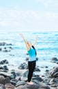 Biracial teen girl on rocks by ocean praising God