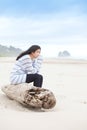 Biracial teen girl sitting on log quietly looking at ocean Royalty Free Stock Photo