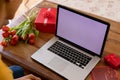 Biracial woman with blank screen laptop on valentine's video call by gifts and flowers