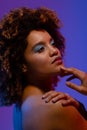 Biracial woman with curly hair and blue eye shadow with hand on chin and shoulder