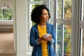 Biracial woman holding cup of coffee and looking out window at home Royalty Free Stock Photo