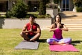 Biracial young couple practicing meditation in prayer pose while sitting on mats in yard