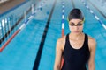 Biracial young female swimmer standing by pool indoors, wearing goggles and cap, copy space Royalty Free Stock Photo