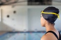 Biracial young female swimmer wearing a black cap is looking at a pool indoors, copy space Royalty Free Stock Photo
