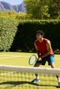 Biracial young man holding tennis racket standing on grassy field at tennis court during sunny day Royalty Free Stock Photo