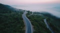 A bird eye scenery view of a winding road cutting turns through clouds of serpentine a dense forest , mountain landscape.Top Down Royalty Free Stock Photo