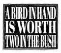 A BIRD IN HAND IS WORTH TWO IN THE BUSH, text on black stamp sign Royalty Free Stock Photo