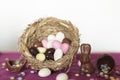 Bird nest with easter almonds, chocolate eggs with sweets and chocolate bunny on pink table