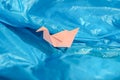 Bird origami of pink paper among a blue plastic bag as if on waves of water or blue sky. Conceptual photo