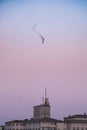 a bird with a parachute and buildings in the background at dusk