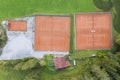 Bird`s eye view to four orange clay tennis courts in green meadow