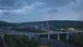 Bird's-eye view. Clip. View of the evening city with a bridge over the river, houses, cars, forest, pipes and a dark