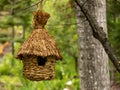 A birdhouse built with hay hanged after a tree