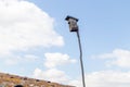 Birdhouse on a wooden stick on the roof against the blue sky with clouds