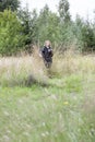 Birds watcher hidden in dry grass, mature woman with binoculars in hand, natural scientist