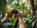 Birdwatcher\'s hands adjusting zoom on portable binoculars, lush forest backdrop, morning light, focused detail Royalty Free Stock Photo