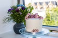 Birthdag cake decorated with pink flowers and a bouguet of flowers in a vase on the windowsill.