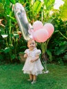 Birthday of baby girl with air balloons in outdoor garden. Happy little child in dress Royalty Free Stock Photo