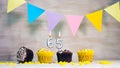 Birthday background with number 65. Beautiful birthday card with colorful garlands, a muffin with a candle burning copyspace. Royalty Free Stock Photo