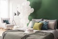 Birthday cake on bed with grey duvet and colorful pillows in bright interior with bunch of white balloons and copy space on Royalty Free Stock Photo