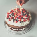 Birthday cake - lighting candles for a girl on a homemade cake with raspberries, blueberries Royalty Free Stock Photo