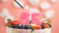 Birthday cake number 65, pink candle on beautiful cake with berries and lighter with fire against background of white