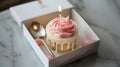 Birthday cake with pink and white icing and lit candle in a box Royalty Free Stock Photo