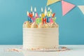 Birthday cake with white cream cheese frosting decorated with multicolored lit happy birthday text shaped candles on a blue Royalty Free Stock Photo