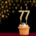 Birthday candle with cupcake - Number 77 on black background with out of focus lights